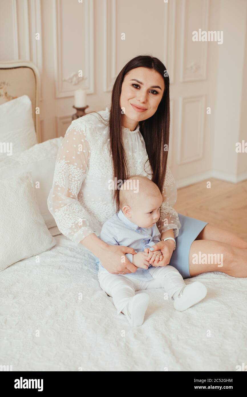 Smiling mother sitting on a bed with her baby son Stock Photo