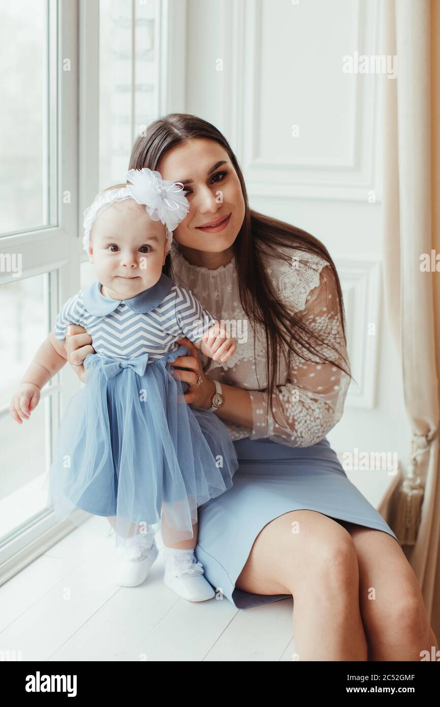 Smiling mother sitting by a window with her baby daughter Stock Photo