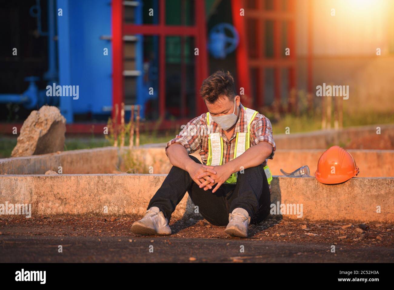 Construction worker wearing a face mask sitting on ground, Thailand Stock Photo