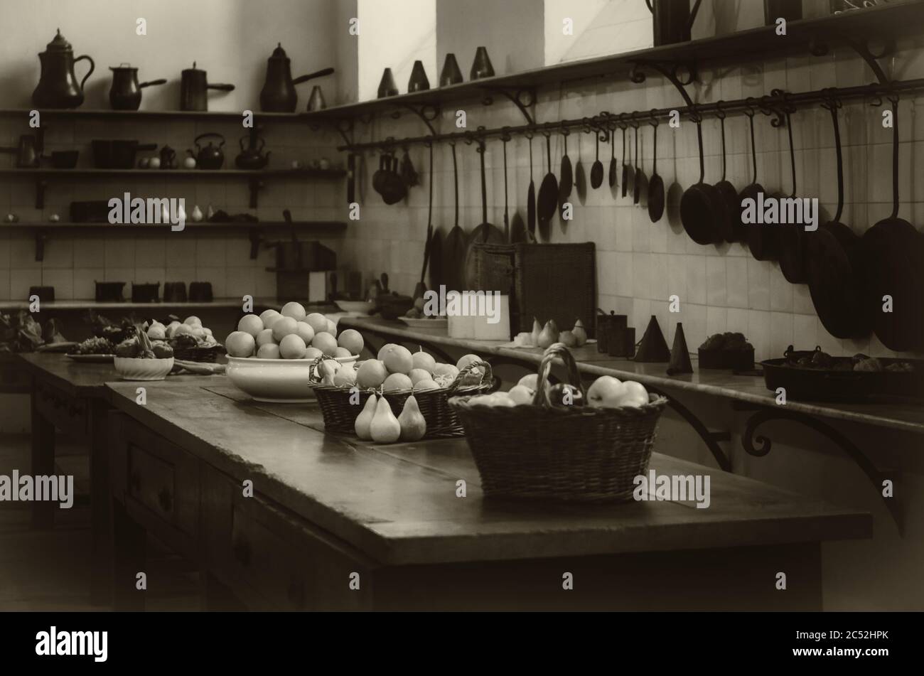 vintage looking image of an antique XIX century old kitchen with tools, pans, pots and food ingredients all over che benches and tables Stock Photo