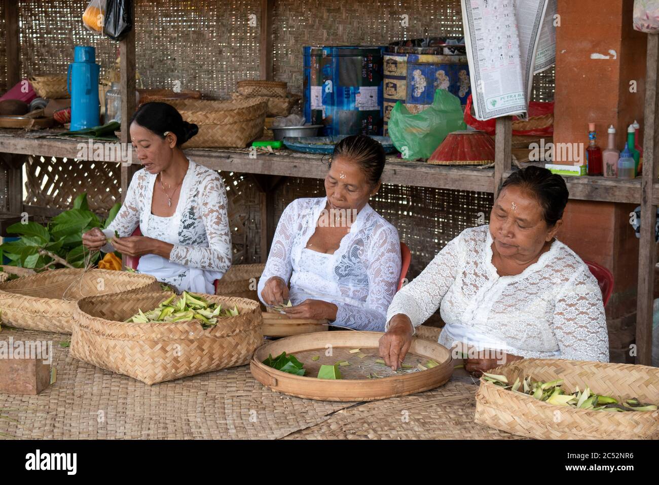 Ubud, Bali / Indonesia: Group of Indonesian women in white hand weaving baskets at a small artisanal shop near the Sacred Monkey Forest. Stock Photo