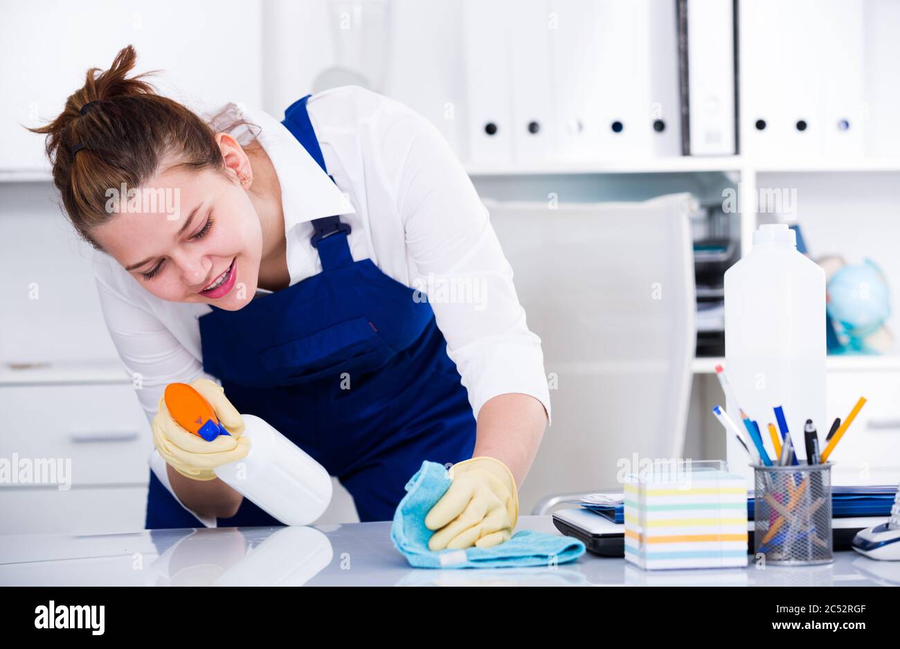 Female office cleaner is cleaning dust from the desk in the office ...