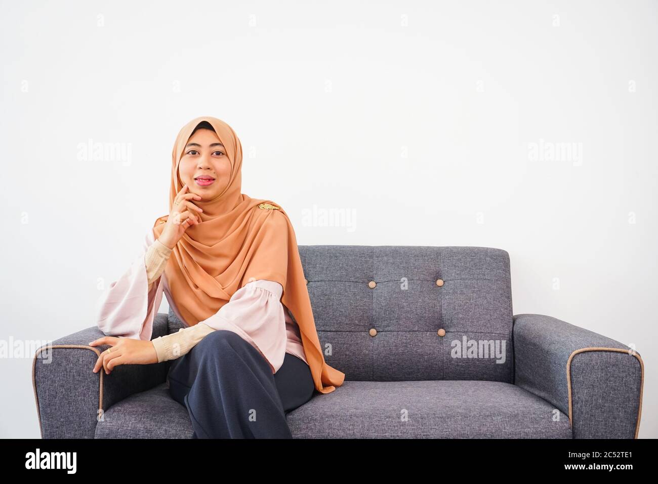Pretty asian muslim woman smiling while sitting on sofa on white background Stock Photo