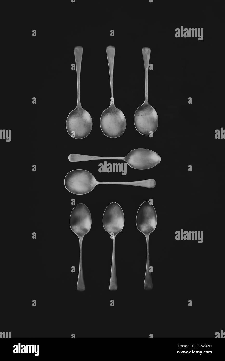 Antique silver spoons laid out in patterns on a dark textured back