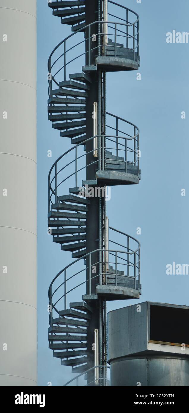 Section of a metal spiral staircase on an industrial building against a blue sky Stock Photo