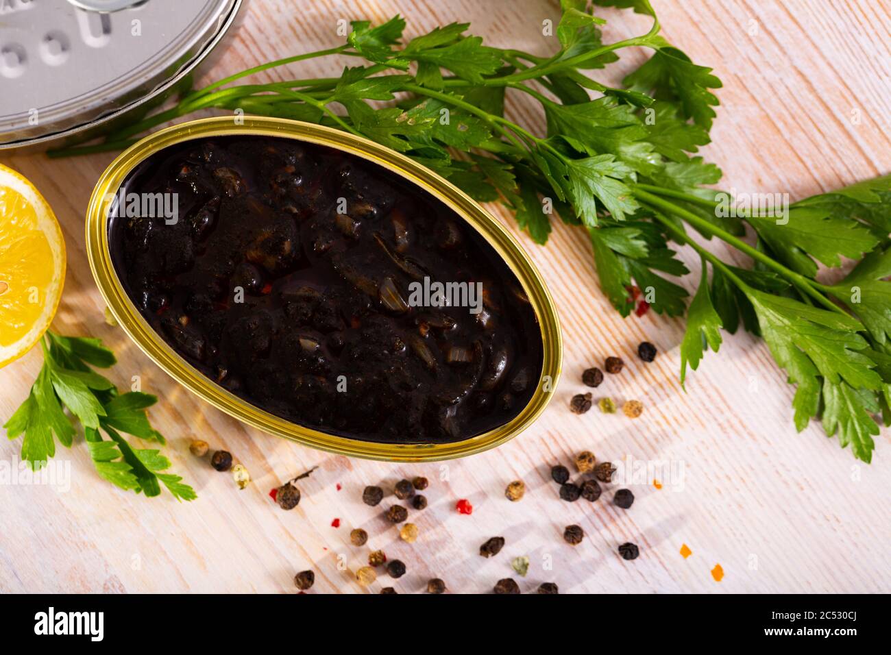 Open can with squid in ink in group of closed cans with seafood, parsley and lemon Stock Photo