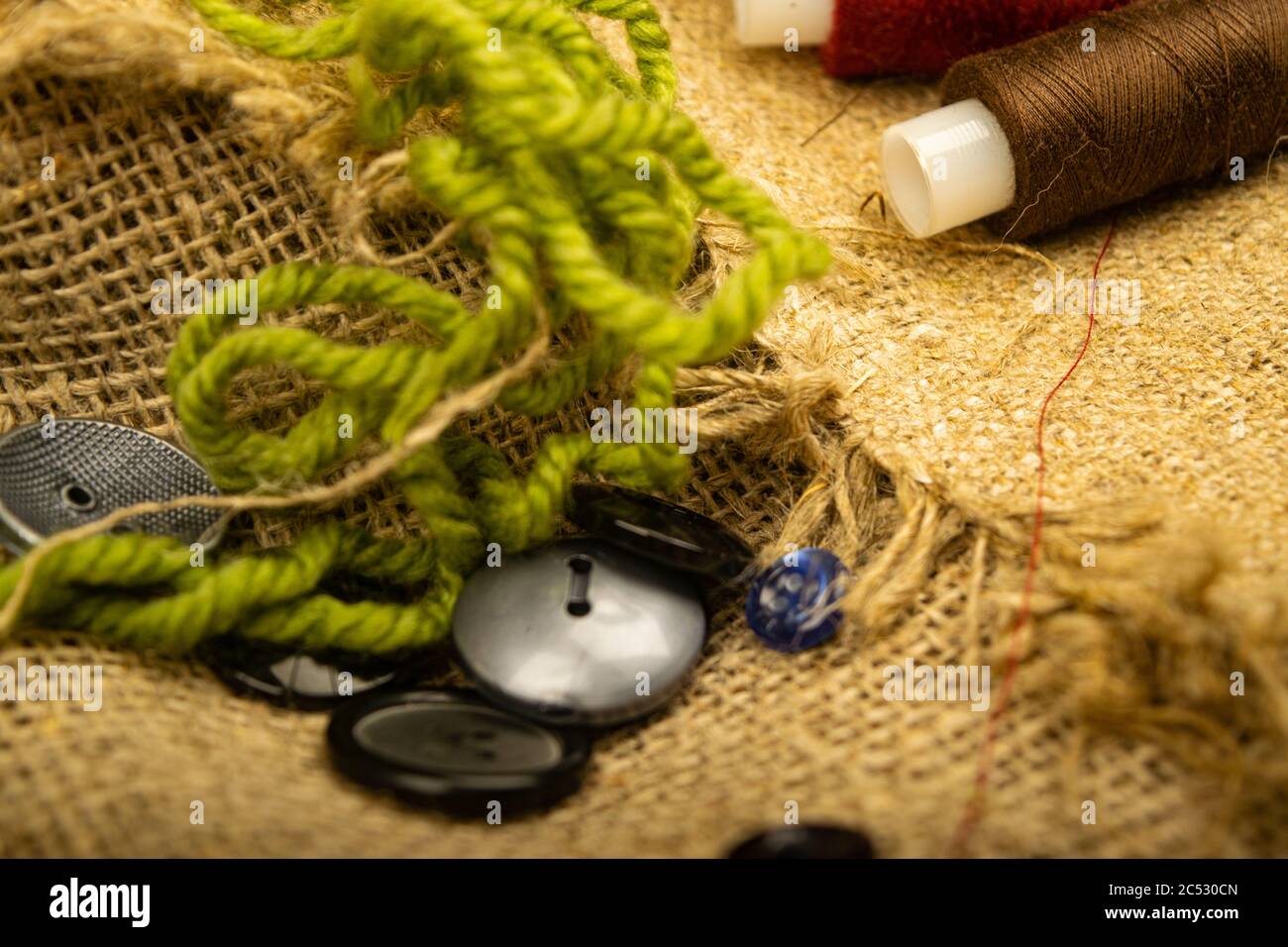 Various buttons and multicolored threads on coarse-textured burlap. Close up Stock Photo