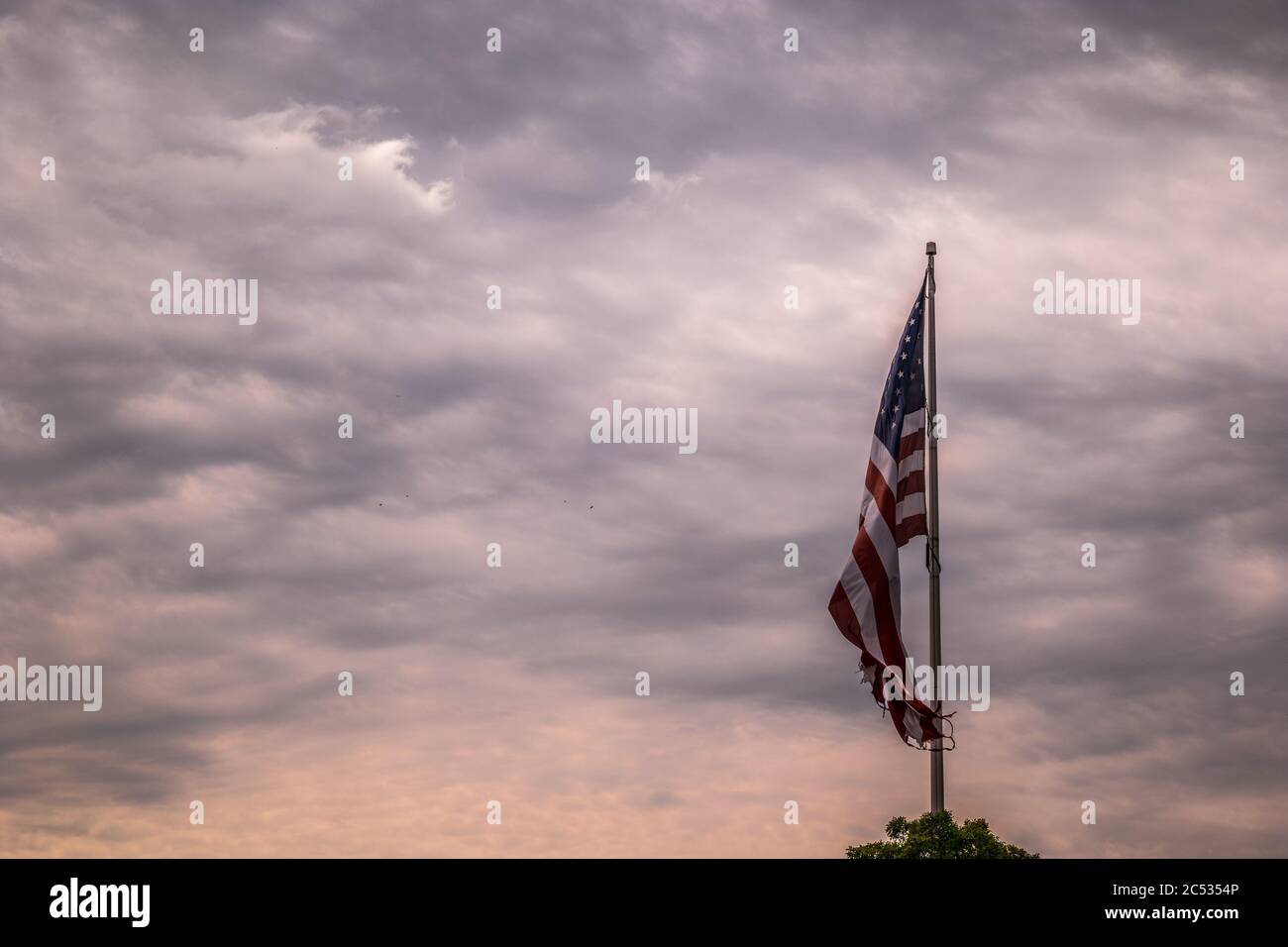 A large American flag flying proudly in the breeze with stormy clouds and birds flying around in the background through the morning skies Stock Photo