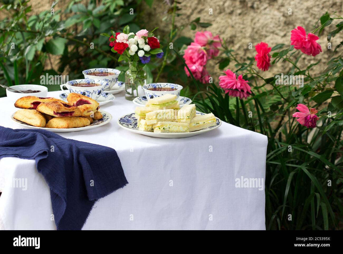 Afternoon tea in the garden with scones, strawberry jam, finger sandwiches with cucumber and egg salad. Stock Photo