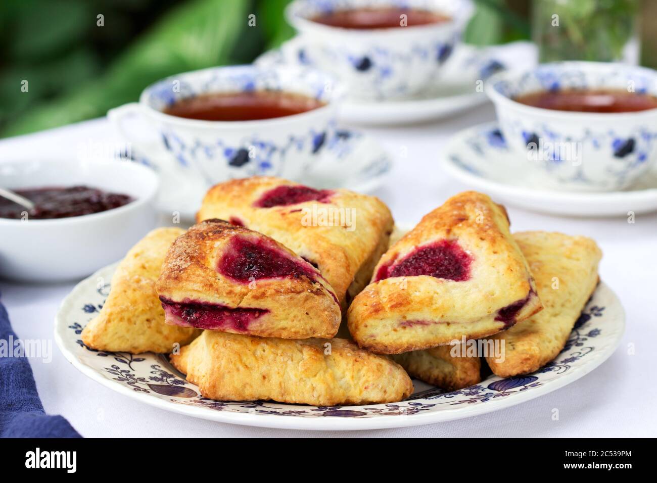 Afternoon tea in the garden with scones, strawberry jam, finger sandwiches with cucumber and egg salad. Stock Photo
