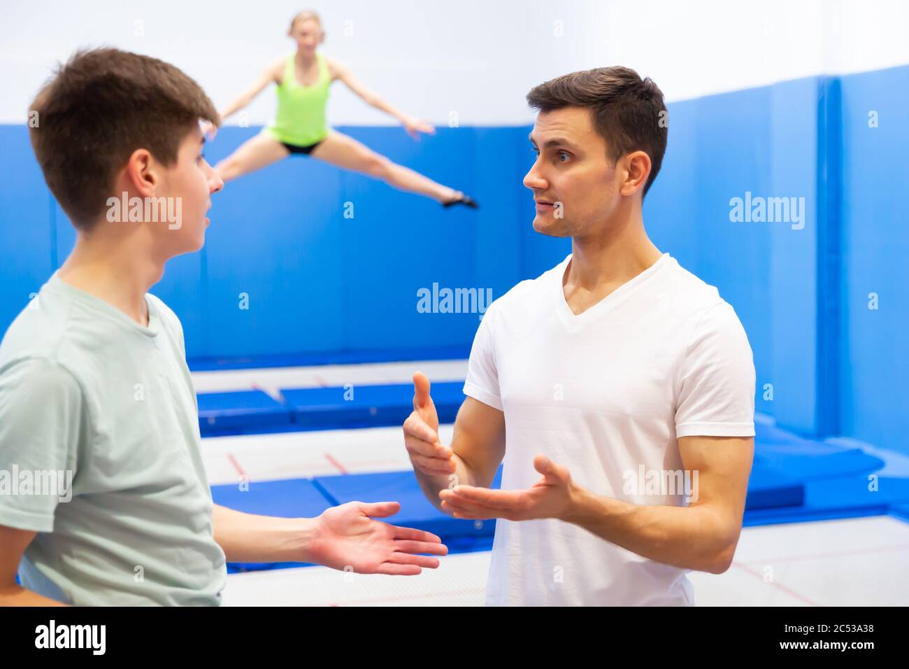 Young trampoline instructor teaching teenage boy of basic jumping