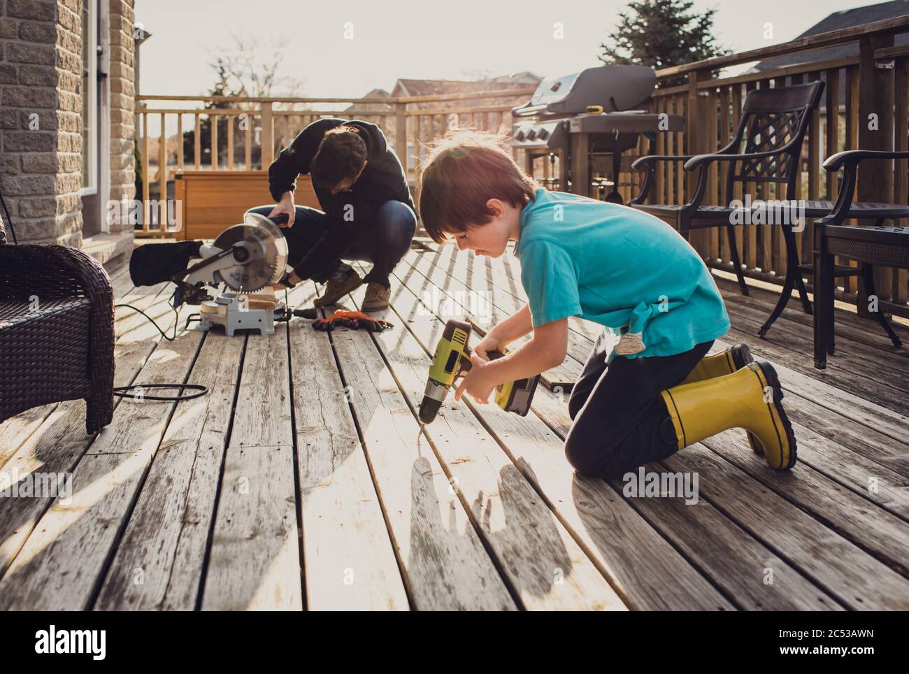 Father and son working on fixing a deck with power tools together Stock