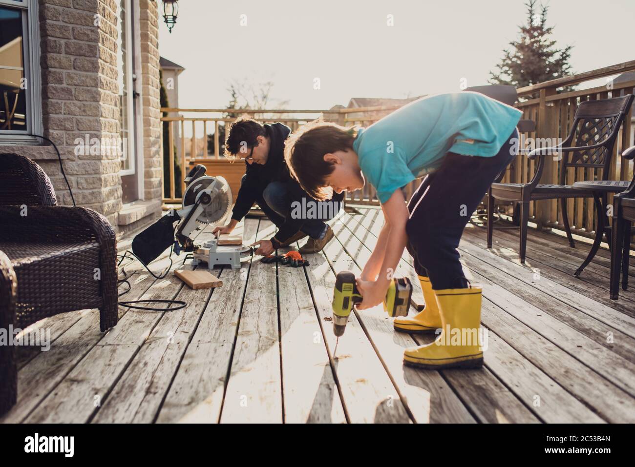 Father and son working on fixing a deck with power tools together Stock
