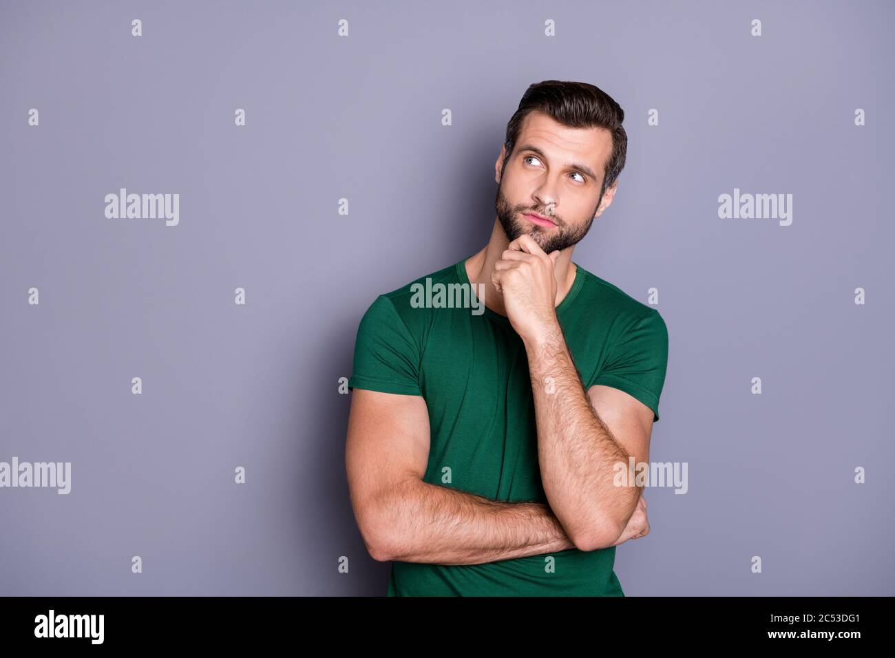 Photo of attractive handsome bearded guy hold arm in chin look up empty space wondered intelligent creative person wear casual green t-shirt isolated Stock Photo
