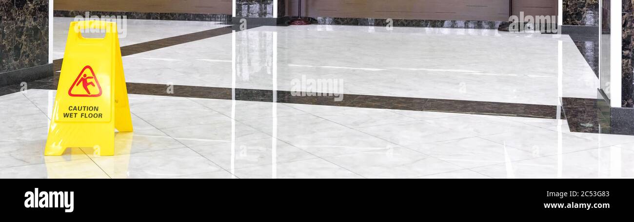 Marble shiny floor in a luxury hallway of company or hotel during cleaning. Panorama of a washed cleaned floor with sign of caution wet floor. Profess Stock Photo