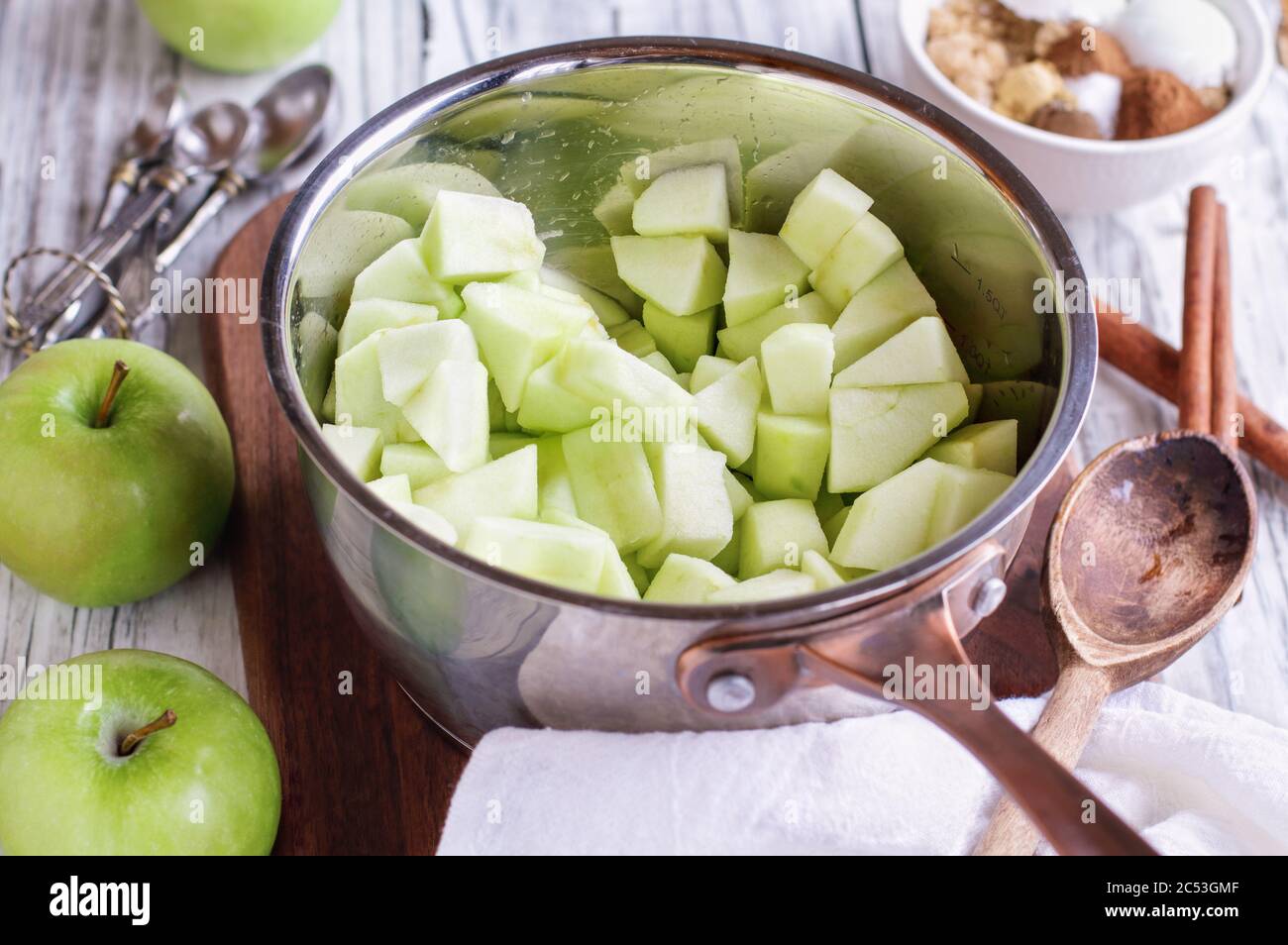Ingredients of freshly diced Granny Smith green apples in a sauce pan with ingredients lying near by to make apple pies or tarts. Selective focus with Stock Photo