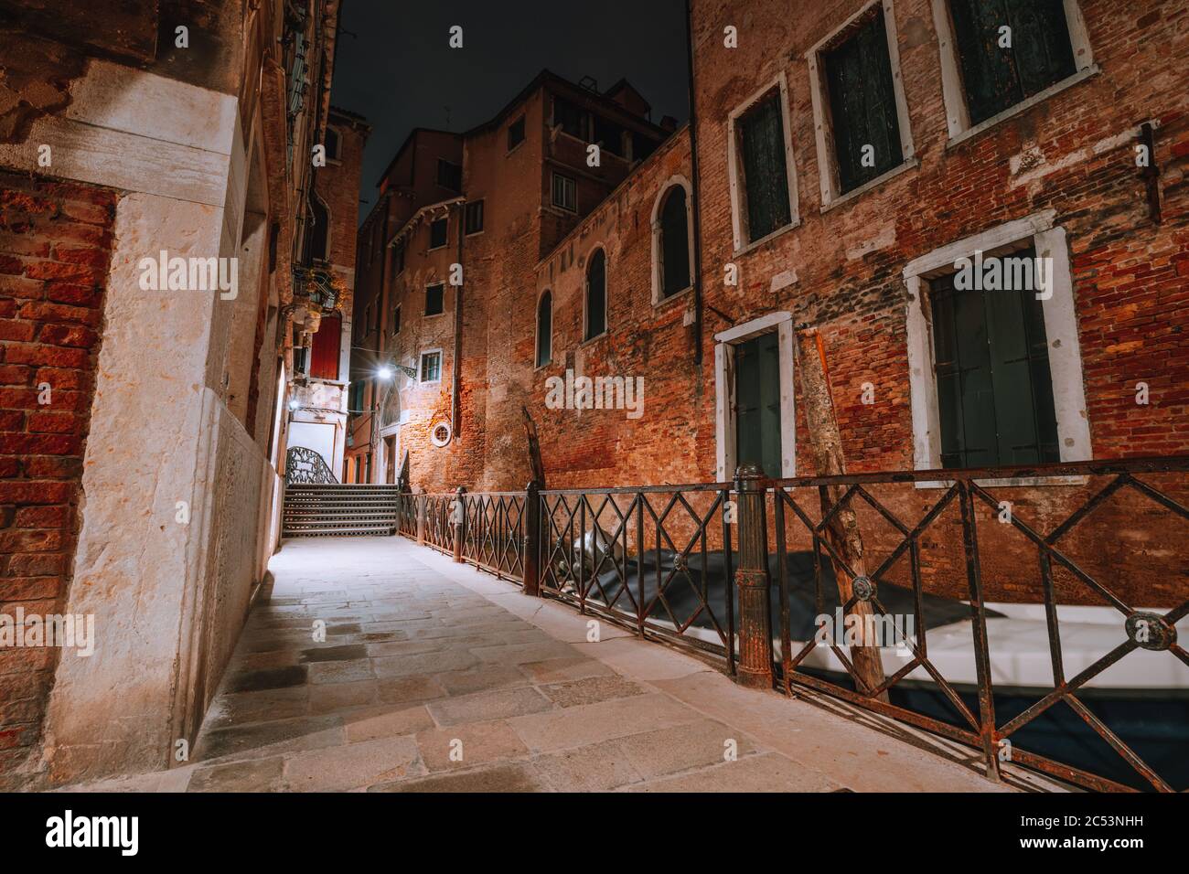 Gothic narrow streets with old red brick wall houses at night. Empty alleyways and bridge stairs in Venice, Italy. Stock Photo