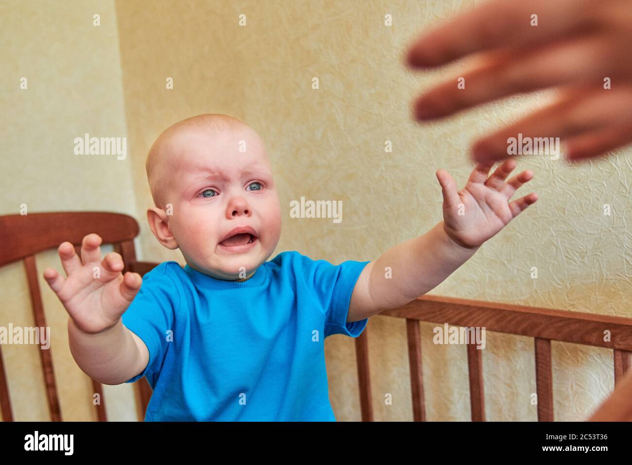 The little boy is crying in the crib and pulling his hands to his mom