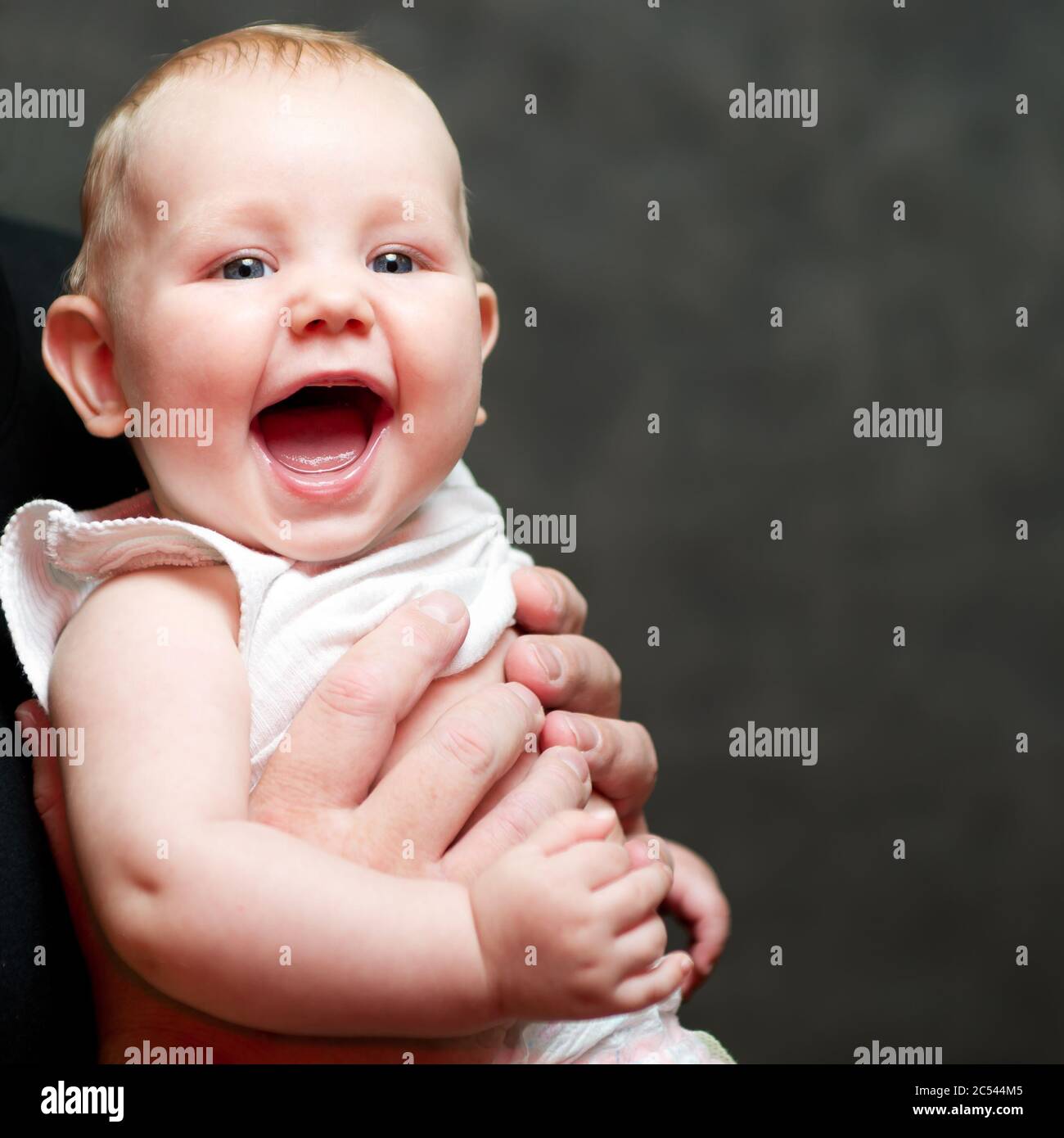 A beautiful smiling baby in the hands of his father Stock Photo