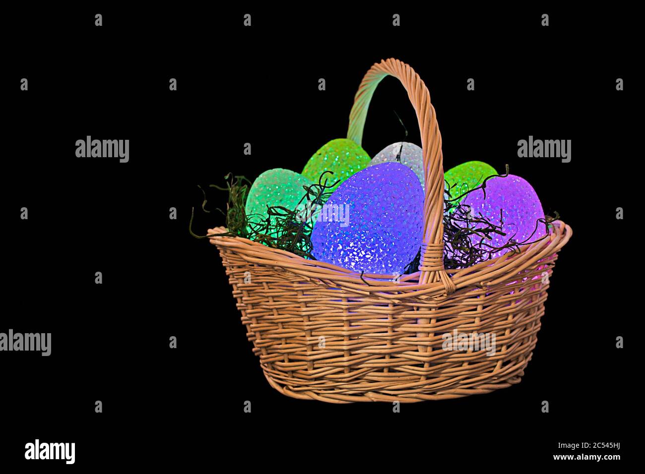 glowing Easter eggs in wicker basket with grass isolated on black Stock Photo