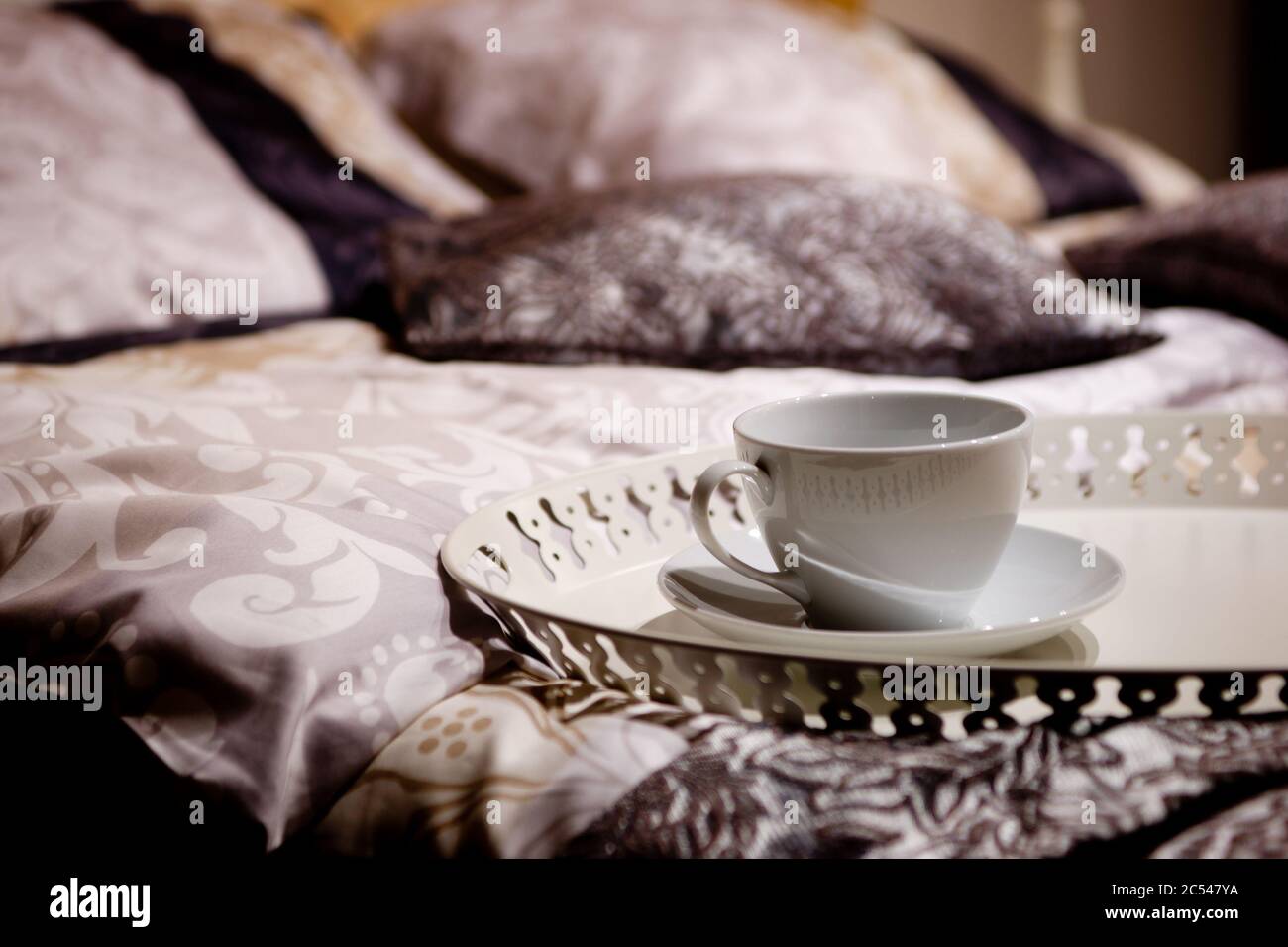 Hotel room interior. Cup of tea or coffee with a tray on a nice bed. Detail of a luxury cozy bedroom. Beautiful linen, sheets and pillows with blurred Stock Photo