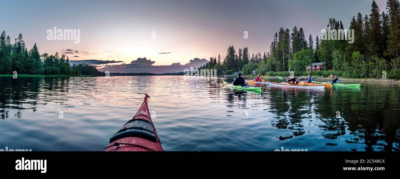 UMEA, SWEDEN - JUNE 26, 2020: group of young people paddling during midnight light in Swedish Lapland, crystal water, night sun, forest, red cabin Stock Photo