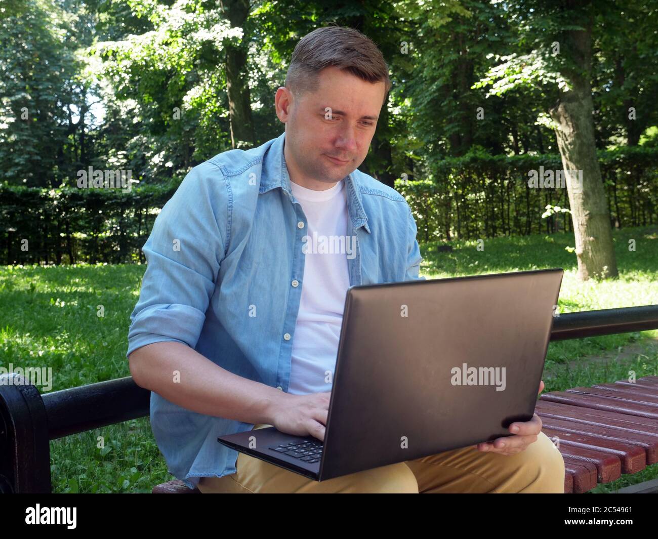 Communication concept. Young guy in the park chatting on the Internet. Stock Photo