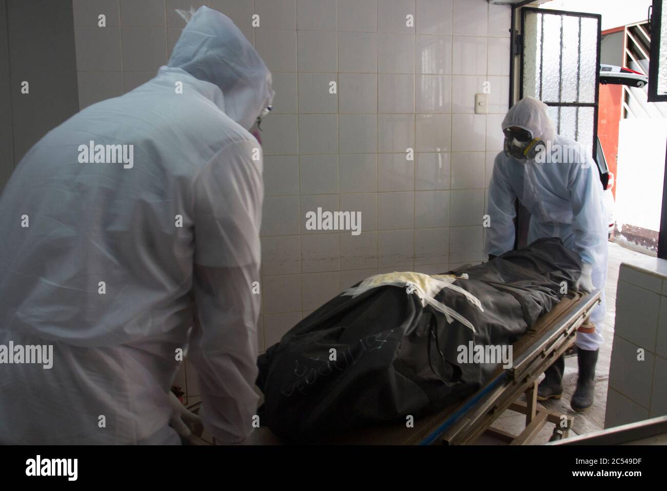 Two workers from Piedra Angel crematory, wearing protection equipment, remove the body of Ricardo Medina Sosa (86), who died in his own bedroom from t Stock Photo