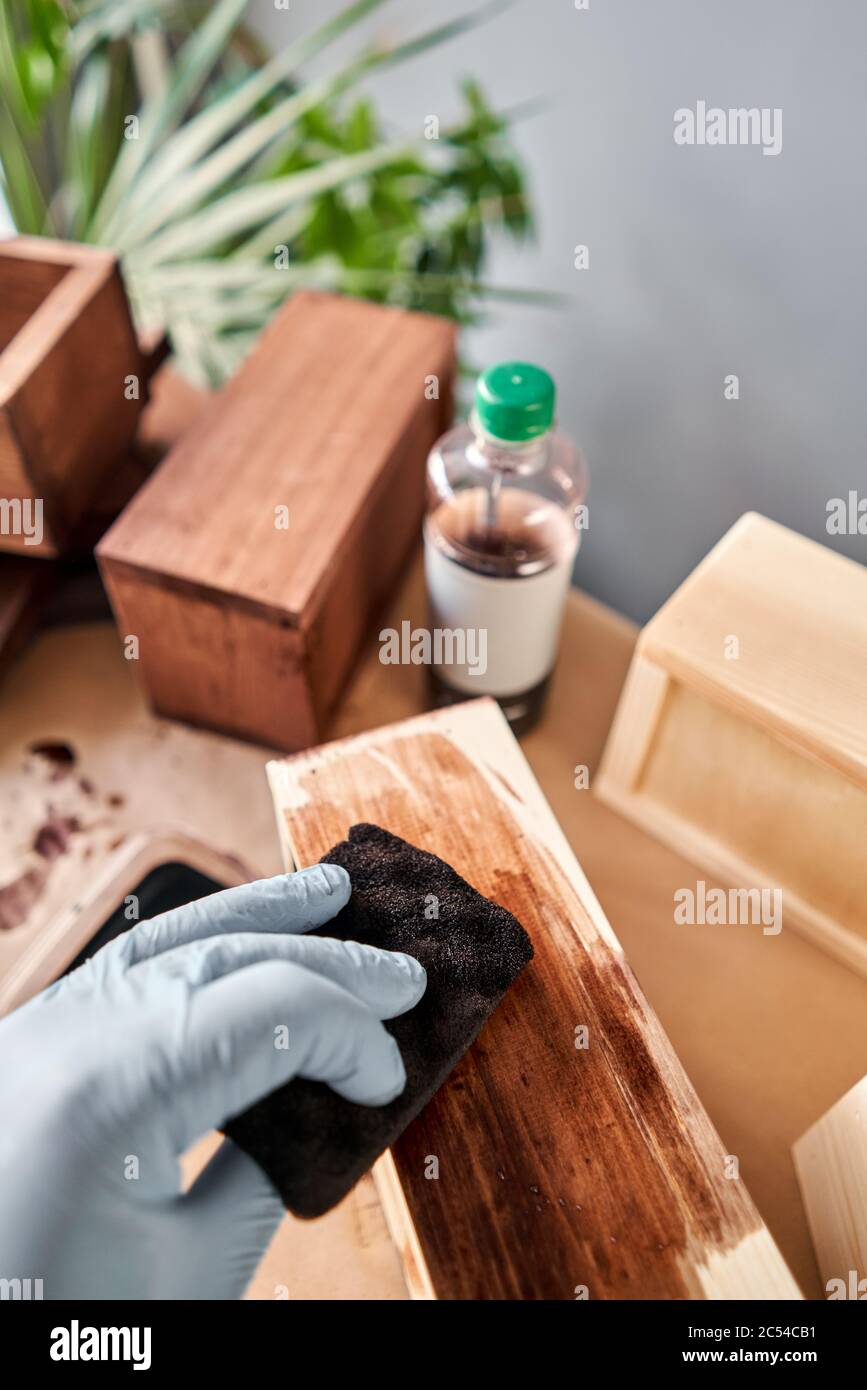 Man carpenter varnishing wooden crate for flowers with brush in her small business woodwork workshop. In your work, do you use stains or wood Stock Photo