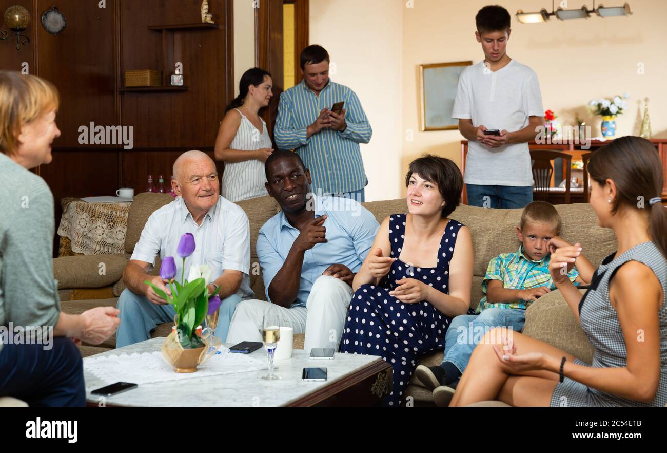 Big happy multiethnic family gathering in parental home, cheerfully talking together in living room Stock Photo