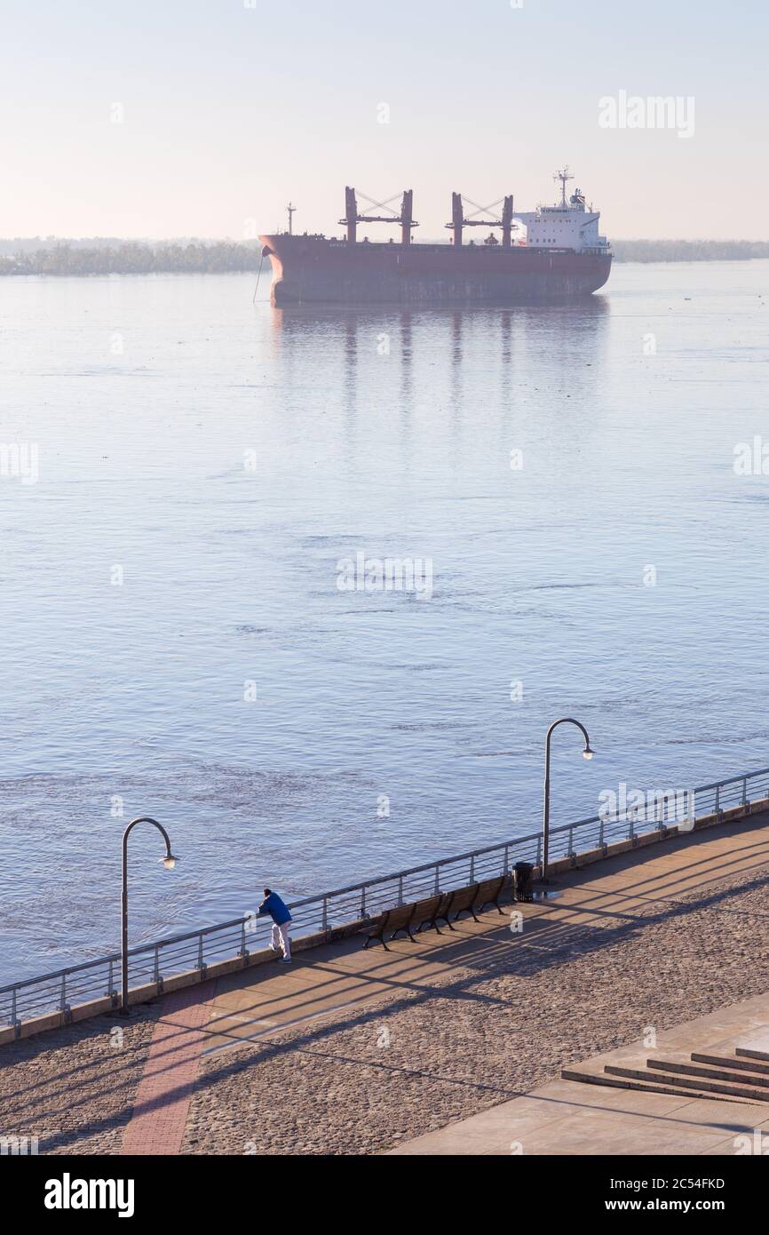 ROSARIO, ARGENTINA. Cargo ship in the Parana river, anchored in front of the coast of Rosario. Man supporting in the railing looking the river. Stock Photo