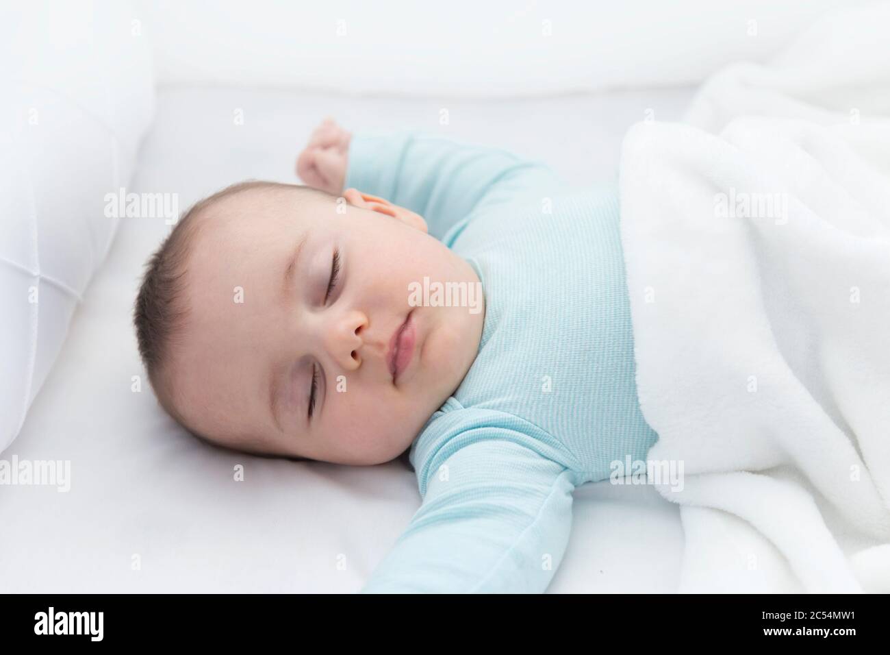 Baby sleeping with a pacifier aside. Light blue pajama and white bed sheets. Stock Photo