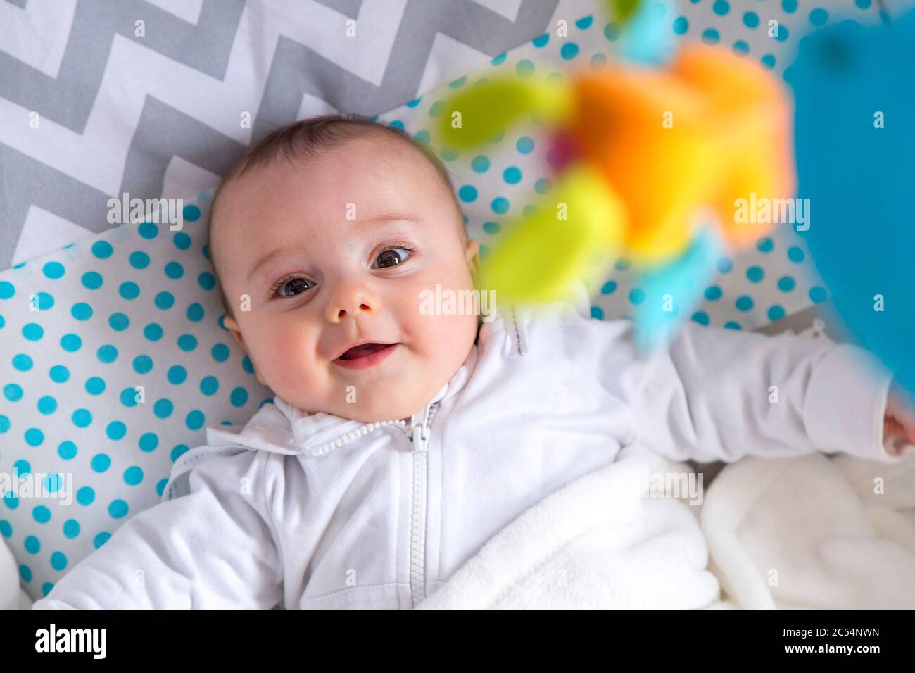 Funny baby boy looking up a mobile in his cradle. Stock Photo