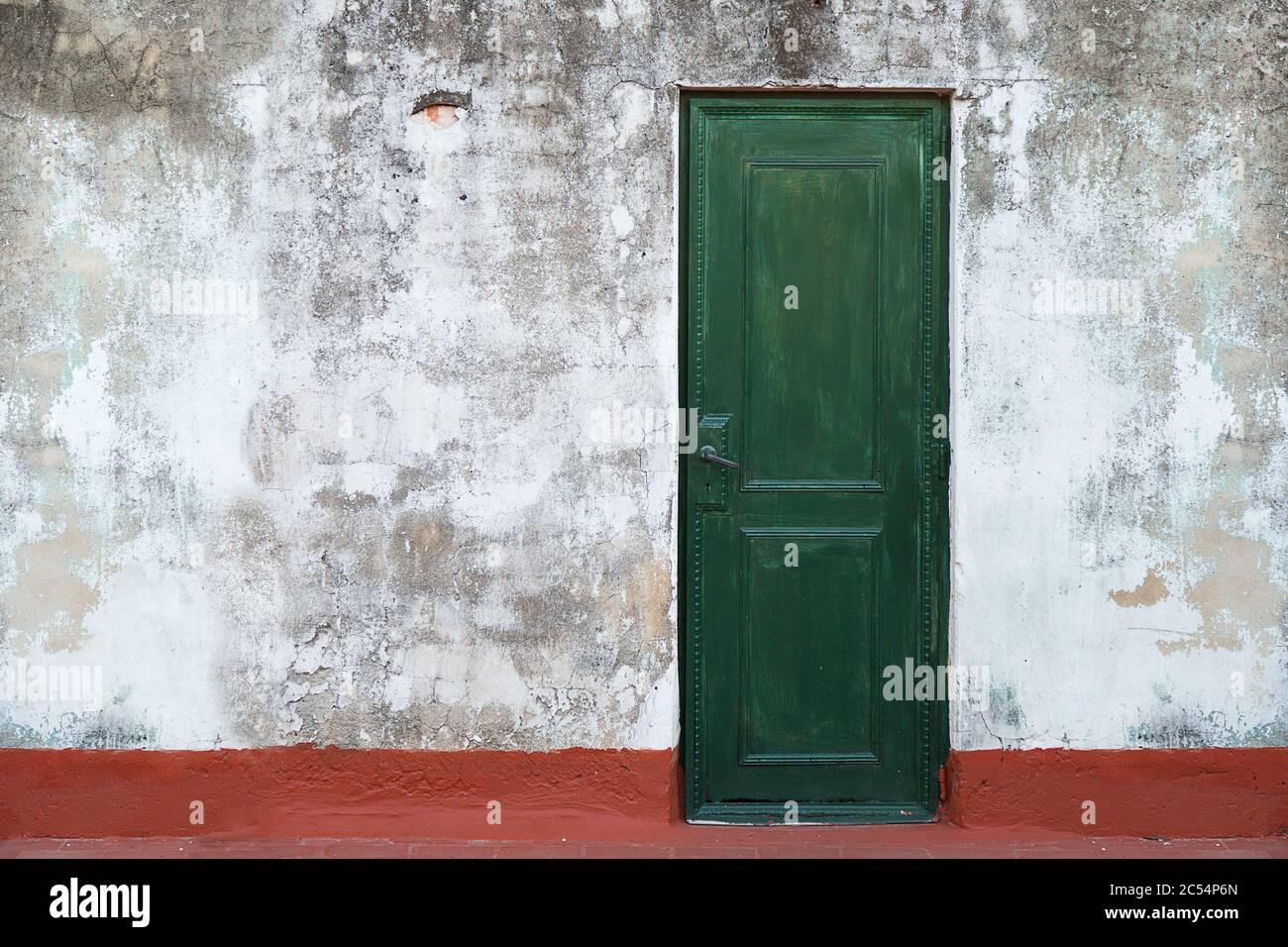 Old green door in a grunge wall. Vintage, retro door. Red floor. Stock Photo