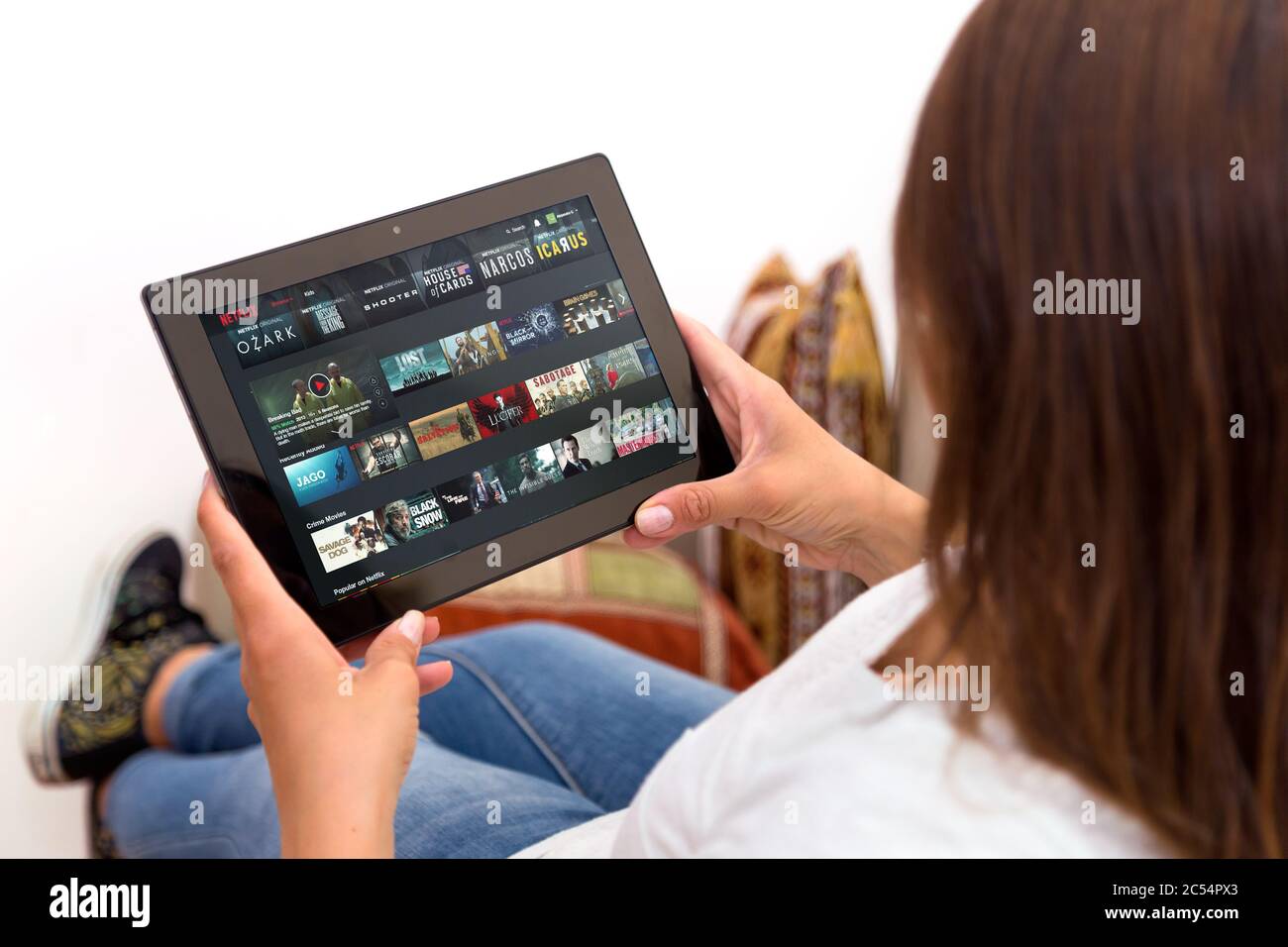 Woman resting in a sofa watching a tablet with netflix on the screen. Stock Photo