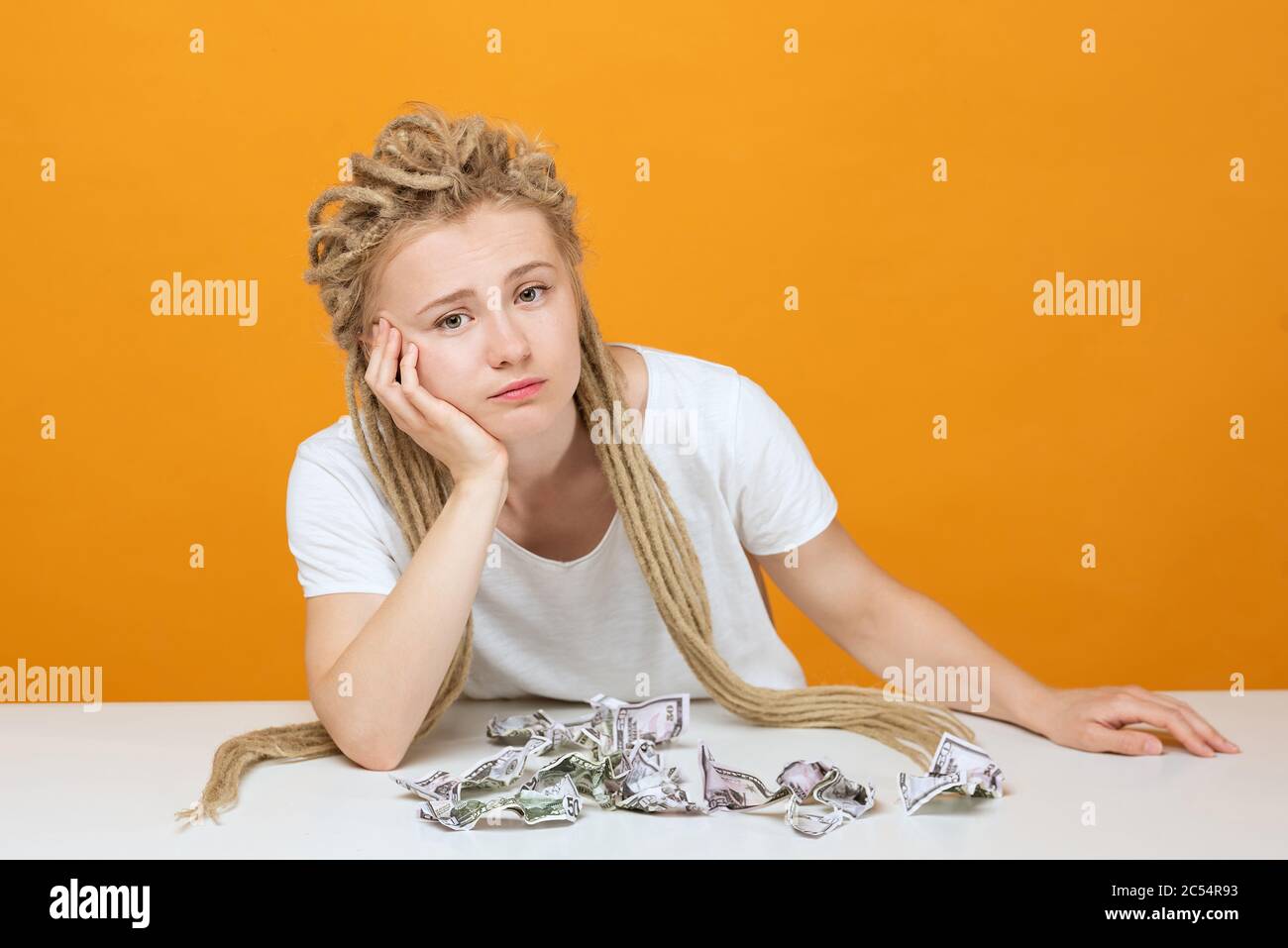 upset girl sitting at table, propped her head on her hand crumpled ...