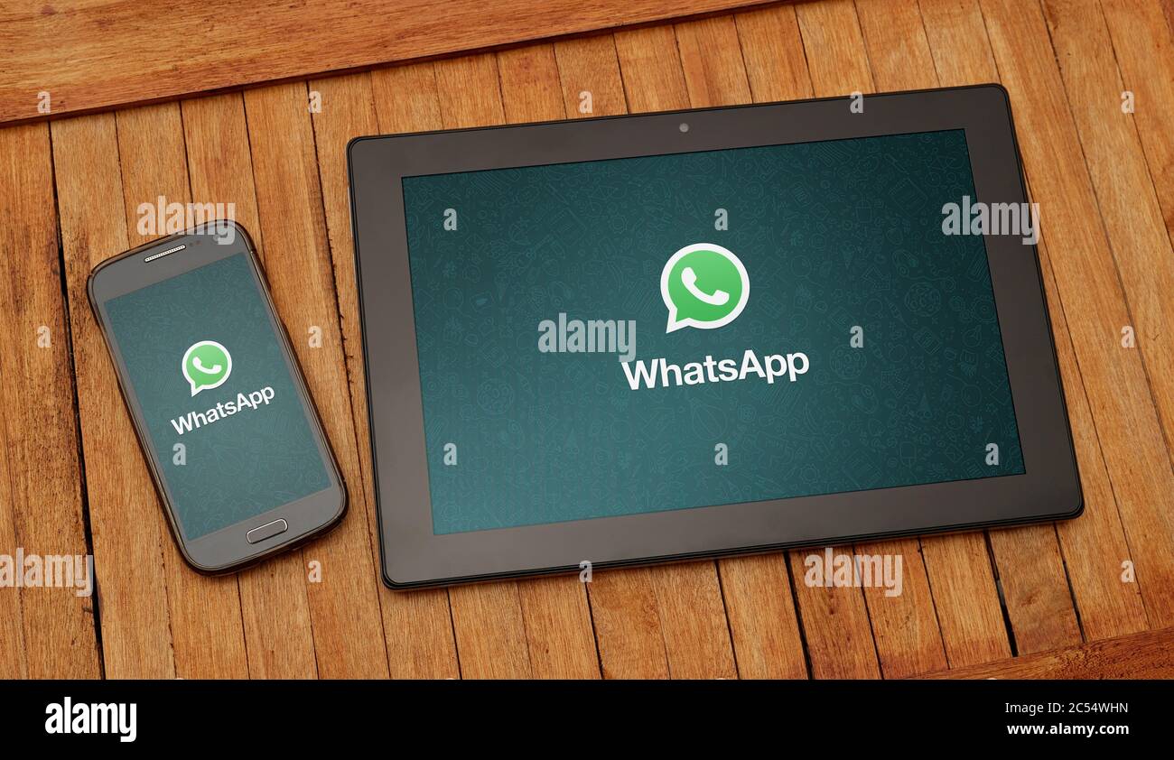 Tablet and cell phone on a rustic table. The Whatsapp application is open on both screens. Stock Photo
