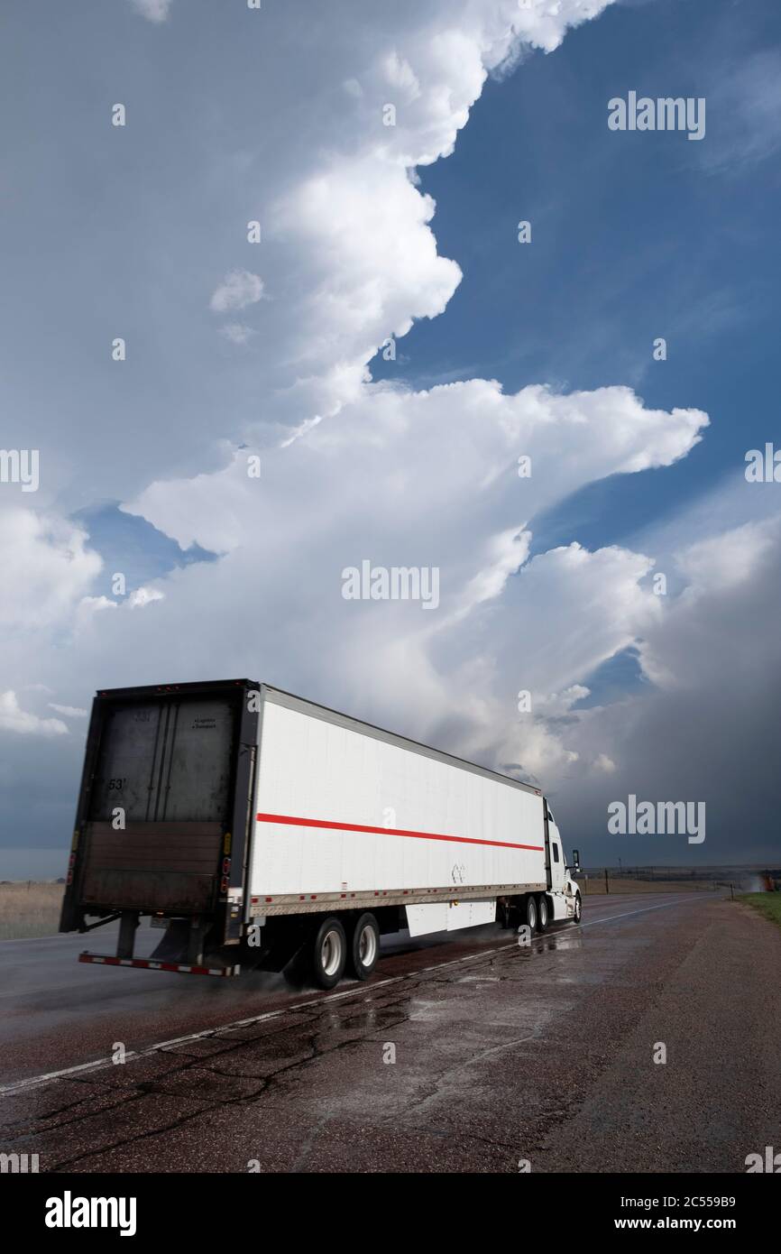 Truck driving along a rural highway on the high plains after a passing storm with thunderheads in the background Stock Photo