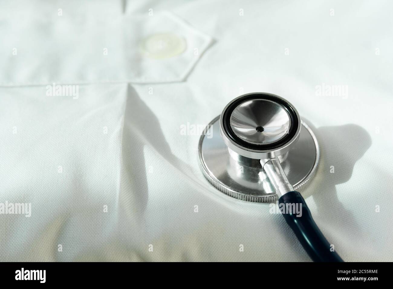 metal stethoscope for medical doctor health diagnosis on white gown suit fabric background Stock Photo