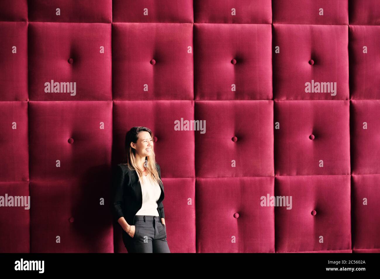 Young Business Woman Standing Against Burgundy Wall Panels Stock Photo