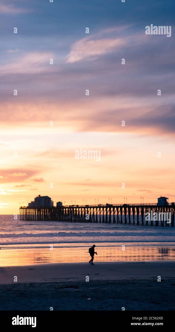 Vertical shot of a silhouette of a pier and a person walking at the ...