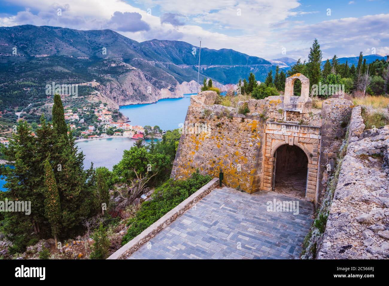 Old fort gate on top of frourio peninsula and Assos village with beautiful sea bay and cypress trees in background. Kefalonia island, Greece. Stock Photo