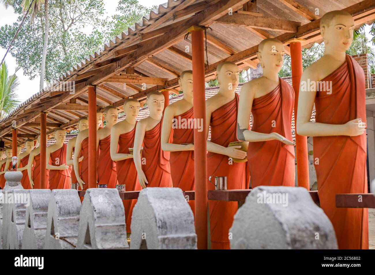Many statues of Buddhist monks stand in a long line on a wall, Sri