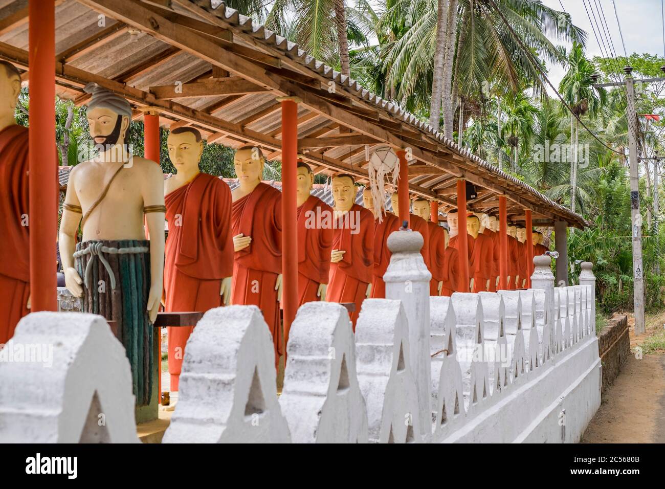 Many statues of Buddhist monks stand in a long line on a wall, Sri
