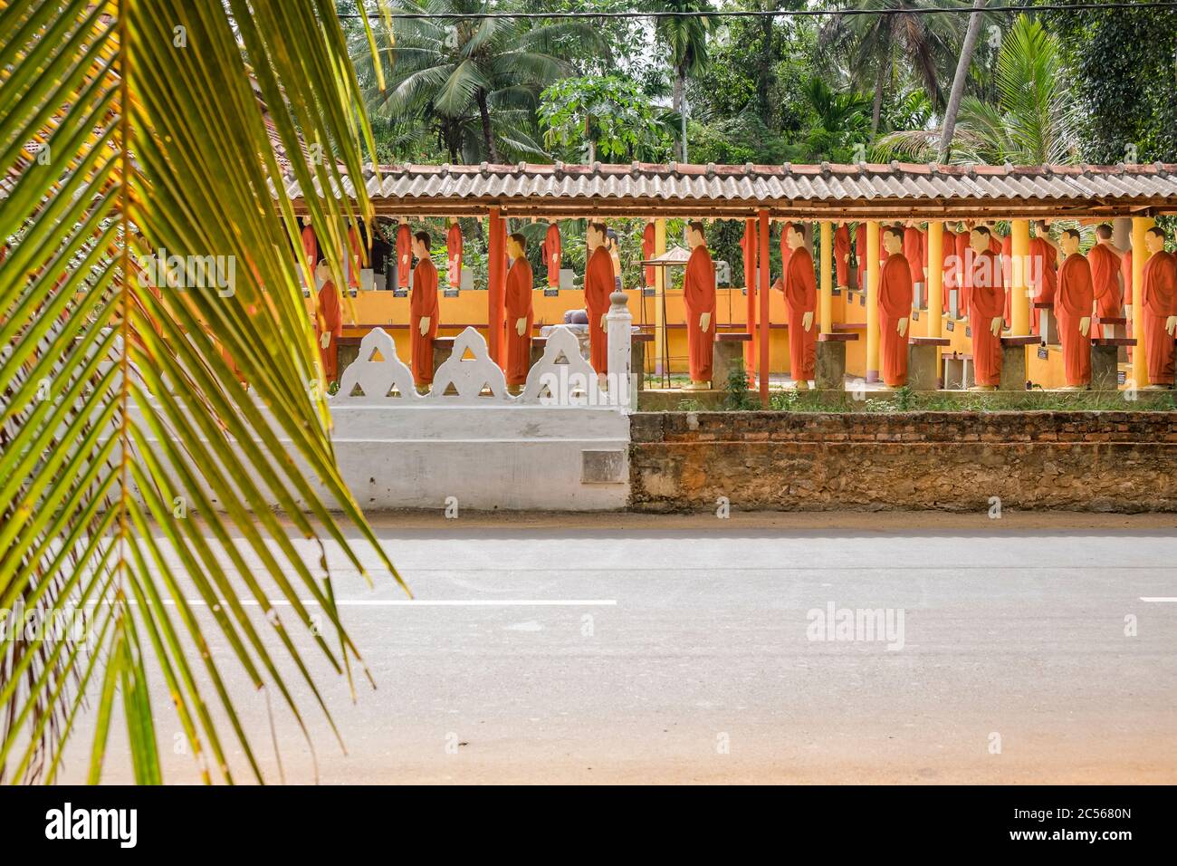 Many statues of Buddhist monks stand in a long line on a wall, Sri