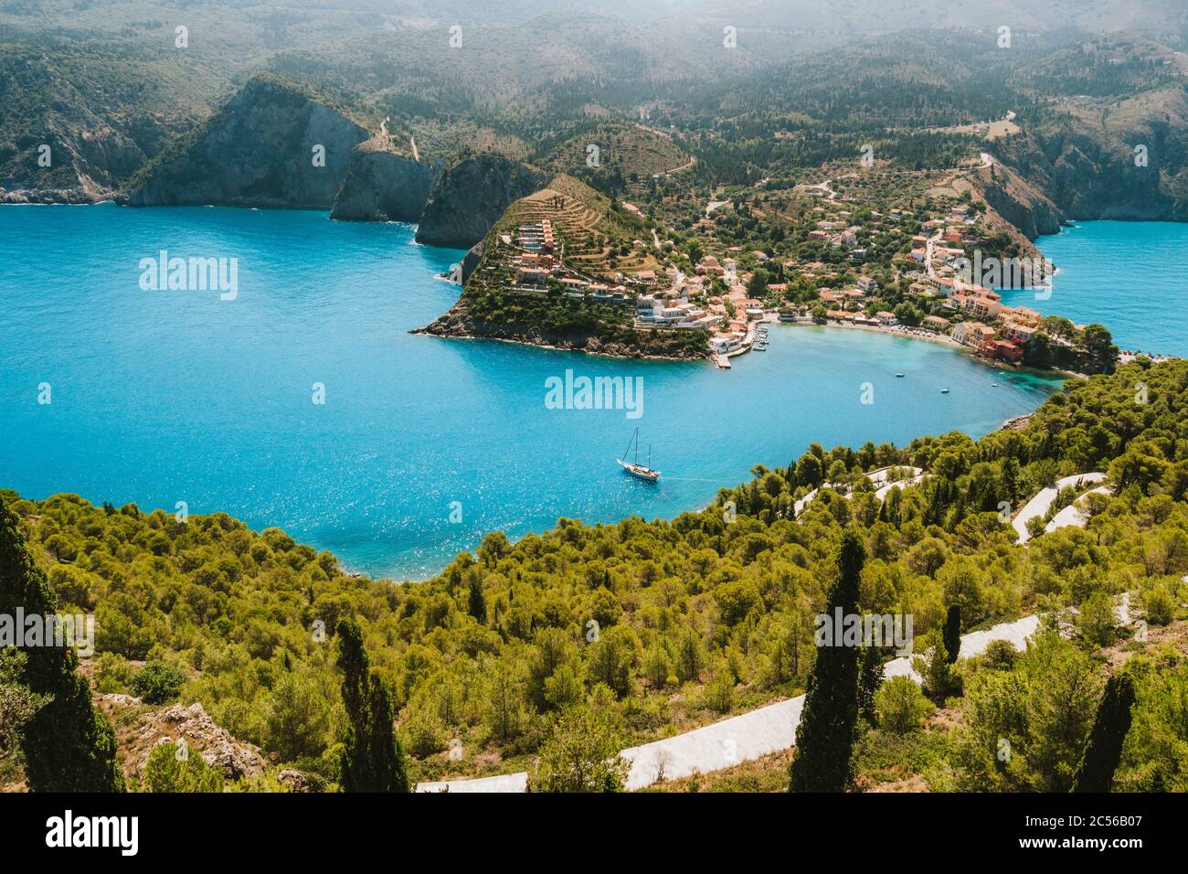 Top view to Assos village. Landmark place of Kefalonia island. Lonely white yacht at anchor in calm beautiful lagoon surrounded by pine and cypress tr Stock Photo