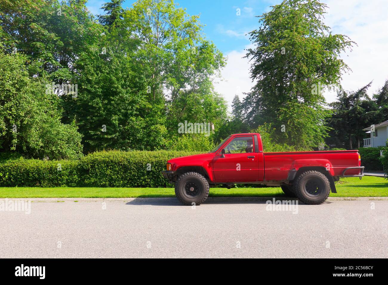 An older red Toyota pickup truck parked on a street with trees in the background. Stock Photo