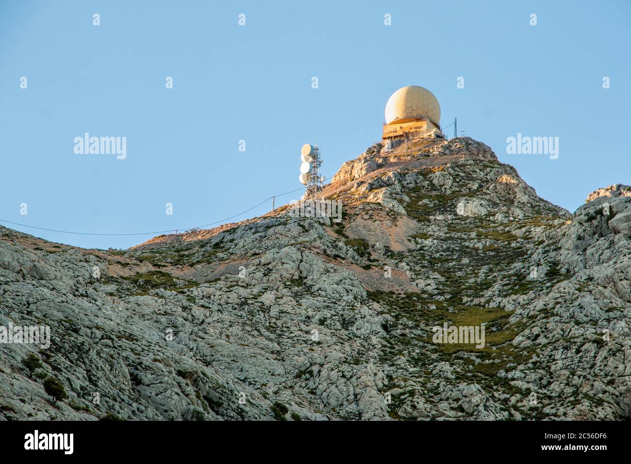 Radar dome station and radio antennas on top of a mountain at sunset ...