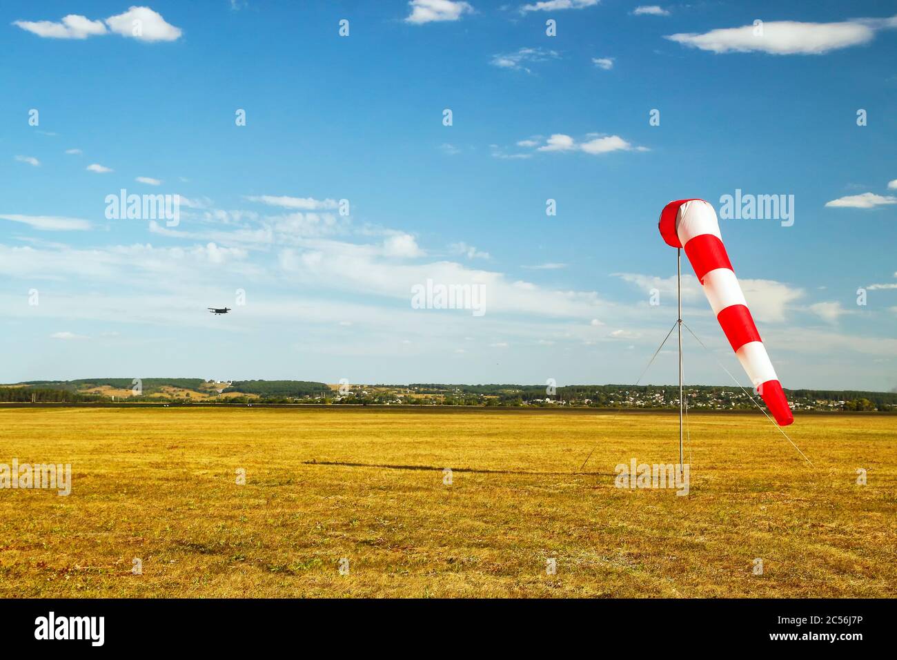 red and white windsock wind sock on blue sky on the aerodrome, yellow field and clouds background Stock Photo