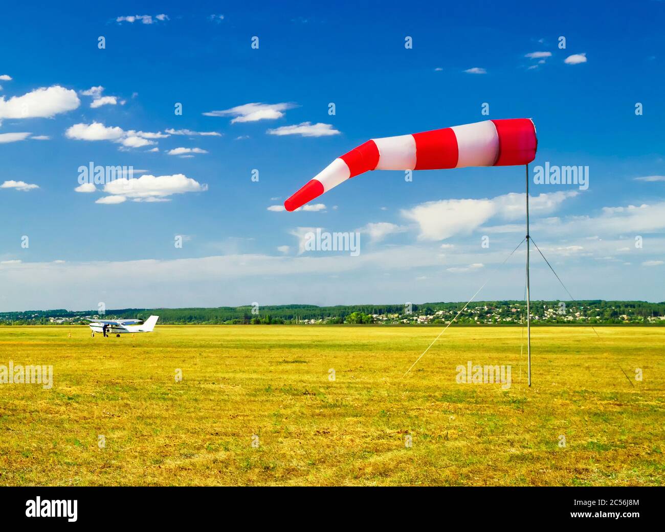 red and white windsock wind sock on blue sky on the aerodrome, yellow field and clouds background Stock Photo